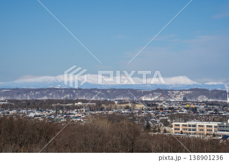 北海道冬・町並みと背景の雪山連峰。北海道の大自然を代表する絶景。白銀に輝く山頂と澄み渡る青空の冬の絶 138901236