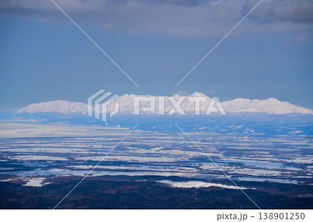 北海道冬・平野の向こうに見える遠景の雪山連峰。北海道の大自然を代表する絶景。白銀に輝く山頂と澄み渡る 北海道冬・平野の向こうに見える遠景の雪山連峰。北海道の大自然を代表する絶景。白銀に輝く山頂と澄み渡る 138901250