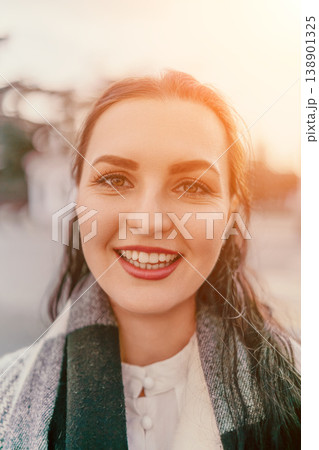 Woman smiling portrait young brunette female wearing a wool scarf during golden hour sunset in an outdoor city setting Woman smiling portrait young brunette female wearing a wool scarf during golden hour sunset in an outdoor city setting 138901325