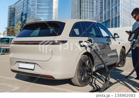 Man charging electric car at charging station while using smartphone in outdoor location Man charging electric car at charging station while using smartphone in outdoor location 138902083