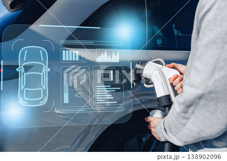 Driver charges electric car at station with battery level display in clear view Driver charges electric car at station with battery level display in clear view 138902096