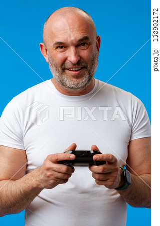 Older man enjoys video games with a controller in a bright blue background setting 138902172
