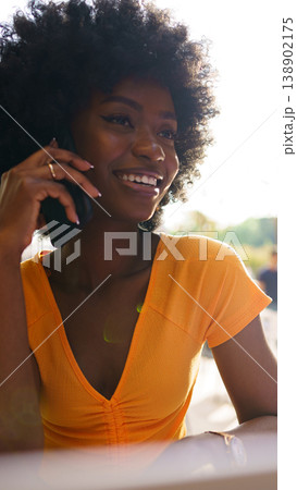 Woman talks on phone outside in sunlight during afternoon social gathering in park Woman talks on phone outside in sunlight during afternoon social gathering in park 138902175