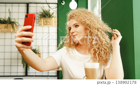 Young woman takes selfie in coffee shop with green walls and light fixtures in background Young woman takes selfie in coffee shop with green walls and light fixtures in background 138902178