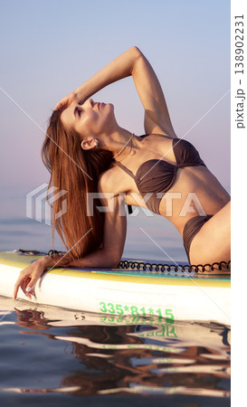 Woman lies on paddleboard in water while enjoying sunset by the beach Woman lies on paddleboard in water while enjoying sunset by the beach 138902231