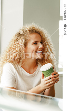 Woman holds a green cup while sitting in a bright cafe during the day 138902246