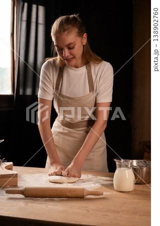 Woman kneading homemade dough on a rustic kitchen table, preparing traditional bread, making fresh pastries 138902760