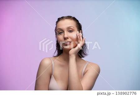 Young woman applying face cream on her cheek, promoting a daily beauty routine for healthy skin on a colorful background with copy space, focusing on skincare and hydration Young woman applying face cream on her cheek, promoting a daily beauty routine for healthy skin on a colorful background with copy space, focusing on skincare and hydration 138902776