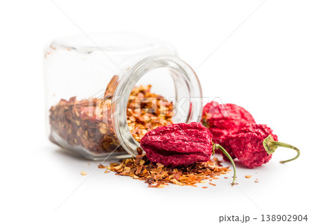 Dried Ghost Peppers and Crushed Chili Flakes Spilling From a Glass Jar on White Background Dried Ghost Peppers and Crushed Chili Flakes Spilling From a Glass Jar on White Background 138902904