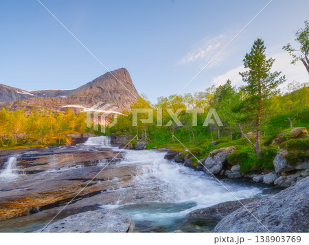 Scenic waterfall flowing from a mountain peak in Norway. Midnight sun. Scenic waterfall flowing from a mountain peak in Norway. Midnight sun. 138903769