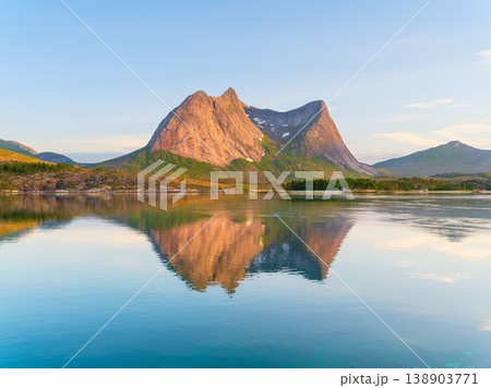 Mountain peaks reflecting in the calm fjord water during midnight sun in Norway. Mountain peaks reflecting in the calm fjord water during midnight sun in Norway. 138903771