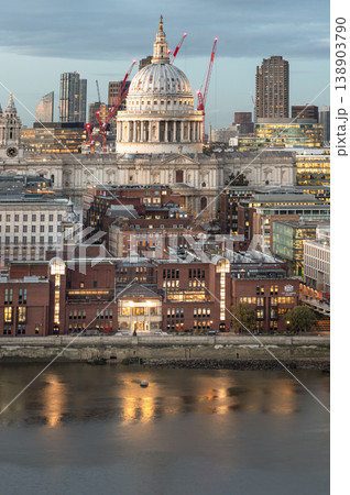 The iconic dome of St. Paul Cathedral rises majestically over the London skyline, a grand testament to history amidst a sea of modern architecture. Warm light glows from the riverside buildings, The iconic dome of St. Paul Cathedral rises majestically over the London skyline, a grand testament to history amidst a sea of modern architecture. Warm light glows from the riverside buildings, 138903790