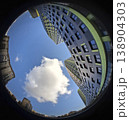 Skyscrapers rise high into the blue sky, with a soft white cloud floating above. This fisheye view shows a modern urban area with tall buildings and open space. 138904303