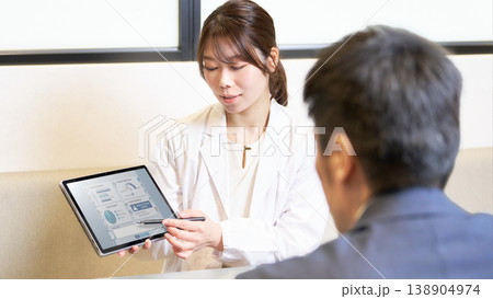タブレットのデータを見せながら社員に説明を行う産業医の女性 138904974