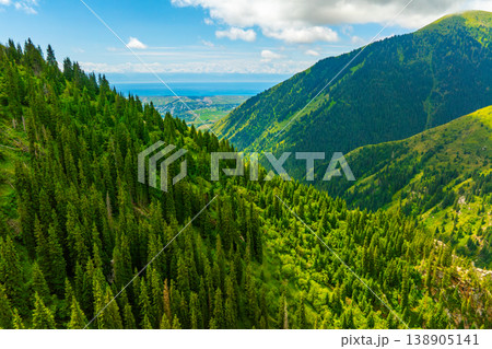 Serene mountain valley with lush forest and distant town in Kyrgyzstan Serene mountain valley with lush forest and distant town in Kyrgyzstan 138905141