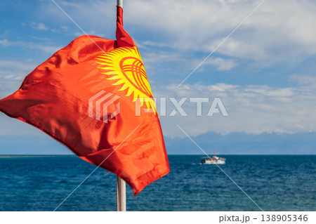 Flag of Kyrgyzstan on boat sailing in water with mountains and clouds Flag of Kyrgyzstan on boat sailing in water with mountains and clouds 138905346