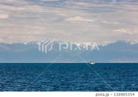 Boat on water on Issyk-Kul lake with people against snow-capped mountains Boat on water on Issyk-Kul lake with people against snow-capped mountains 138905354