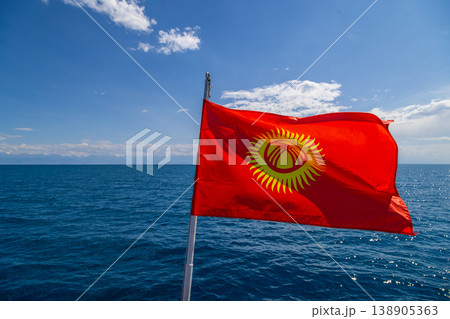 National flag of Kyrgyzstan waving on pole by serene lake with mountains in background National flag of Kyrgyzstan waving on pole by serene lake with mountains in background 138905363