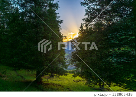 Majestic sunset over mountains and forest in Kyrgyzstan, view between trees Majestic sunset over mountains and forest in Kyrgyzstan, view between trees 138905439