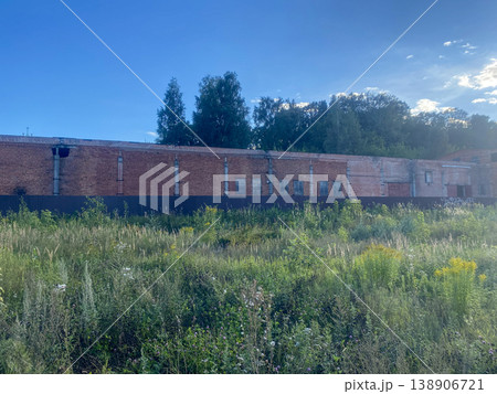 Old brick building stands amid tall grass and trees under a blue sky in late afternoon light 138906721