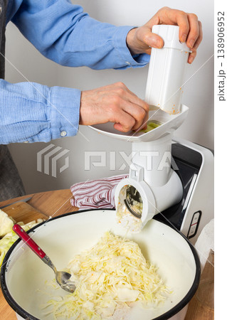 A 53-year-old man prepares cabbage and carrots for fermentation in his kitchen. He uses a machine to shred the vegetables while surrounded by kitchen tools and ingredients A 53-year-old man prepares cabbage and carrots for fermentation in his kitchen. He uses a machine to shred the vegetables while surrounded by kitchen tools and ingredients 138906952