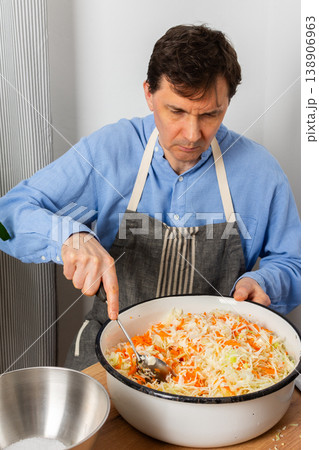 A 53-year-old man mixes cabbage and carrots in a large bowl in his kitchen while preparing for fermentation using simple tools and ingredients A 53-year-old man mixes cabbage and carrots in a large bowl in his kitchen while preparing for fermentation using simple tools and ingredients 138906963
