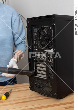 A 53-year-old man cleans dust from a computer system unit with a vacuum cleaner in a tidy room. He carefully removes dirt to keep the device running well A 53-year-old man cleans dust from a computer system unit with a vacuum cleaner in a tidy room. He carefully removes dirt to keep the device running well 138907022