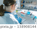 A woman scientist works at a computer, examining scientific data visualizations and laboratory test results. The scene highlights innovation, research, and technology in a bright, modern lab setting 138908144