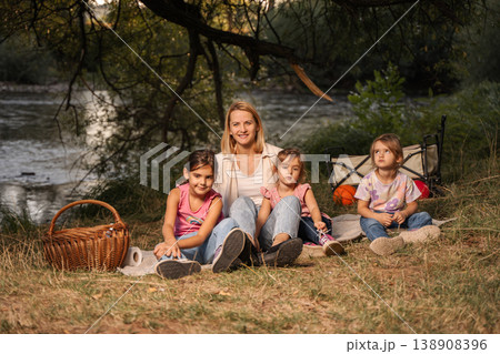 Mother and daughters enjoying a picnic by the river Mother and daughters enjoying a picnic by the river 138908396