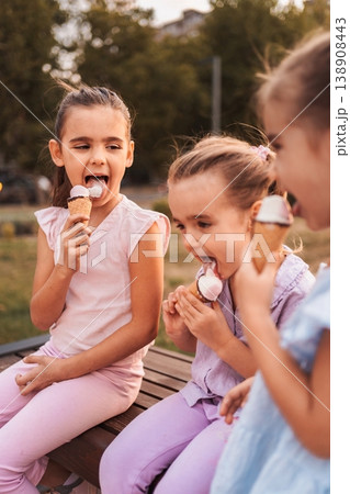 Three little girls enjoying ice cream cones in a park Three little girls enjoying ice cream cones in a park 138908443