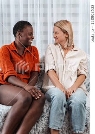 Two young women smiling and talking, sitting on a sofa Two young women smiling and talking, sitting on a sofa 138908532