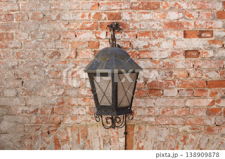 Vintage black metal lantern hanging against a weathered red brick wall 138909878