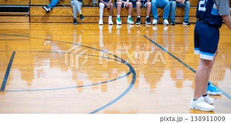 Basketball players prepare for the game in a gym during a youth sports event with fans in the background and a polished wooden floor Basketball players prepare for the game in a gym during a youth sports event with fans in the background and a polished wooden floor 138911009