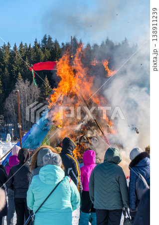 Fire burns straw doll during Maslenitsa festival. People watch fire at winter festival in snowy place 138911239