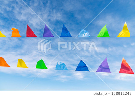 Colorful triangular festival flags hanging on lines against wispy clouds sky 138911245