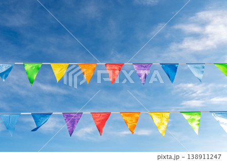 Colorful festive pennant flags hanging under bright wispy clouds sky Colorful festive pennant flags hanging under bright wispy clouds sky 138911247