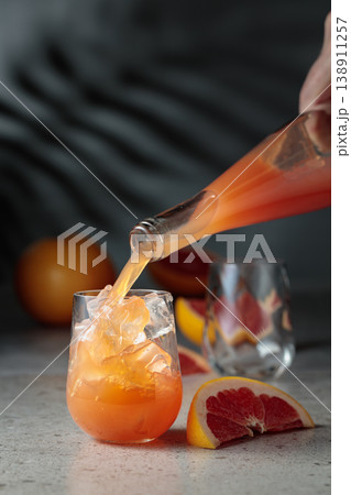 Grapefruit juice is poured into a glass with ice. Grapefruit juice is poured into a glass with ice. 138911257