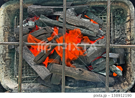 Close up view of glowing charcoal briquettes with vibrant orange flames in a grill Close up view of glowing charcoal briquettes with vibrant orange flames in a grill 138912190
