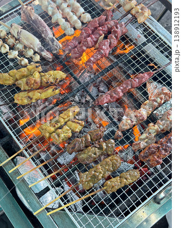 Assortment of skewered meats and seafood grilling over hot coals at an outdoor stall 138912193