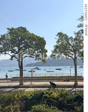 Scenic coastal path with cyclist and sailboats on a clear sunny day Scenic coastal path with cyclist and sailboats on a clear sunny day 138912195