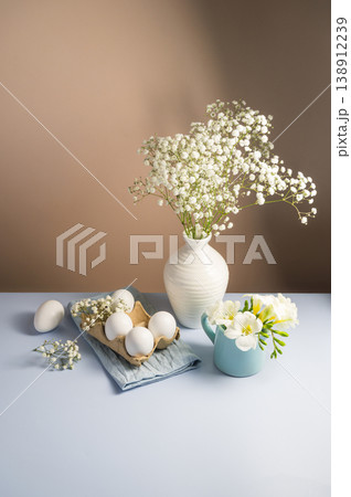 Easter eggs background. White eggs in cardboard box and gypsophila flowers in a vase. Spring holiday Easter eggs background. White eggs in cardboard box and gypsophila flowers in a vase. Spring holiday 138912239
