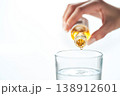 Hand delicately pouring liquid drop into a clear glass on a bright background 138912601
