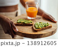 Hands holding a wooden plate with green spread toast and a fresh drink 138912605
