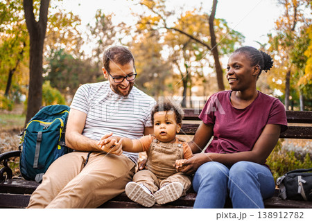 Mixed race couple is sitting on a park bench with their son 138912782