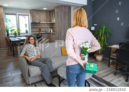 Blonde smiling woman surprises her best friend with a gift and flowers Blonde smiling woman surprises her best friend with a gift and flowers 138912830