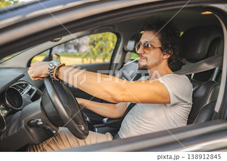 Man with curly hair driving a car and smoking a cigarette 138912845