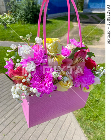 Colorful flower basket with pink handle and fresh flowers in various colors on a sunny day 138912893