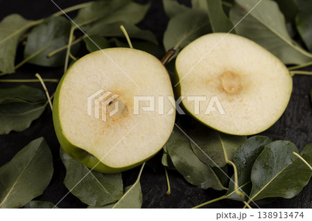a ripe juicy sliced pear lies on the table with the green foliage of the pear, a large number of green leaves of the pear tree and a ripe covered pear with a red-green peel cut in half a ripe juicy sliced pear lies on the table with the green foliage of the pear, a large number of green leaves of the pear tree and a ripe covered pear with a red-green peel cut in half 138913474