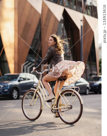 Young woman cycling on city street on a windy day Young woman cycling on city street on a windy day 138913616