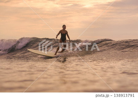 Woman Joyfully Dances Atop Surfboard During Sunset Amidst Gentle Waves 138913791